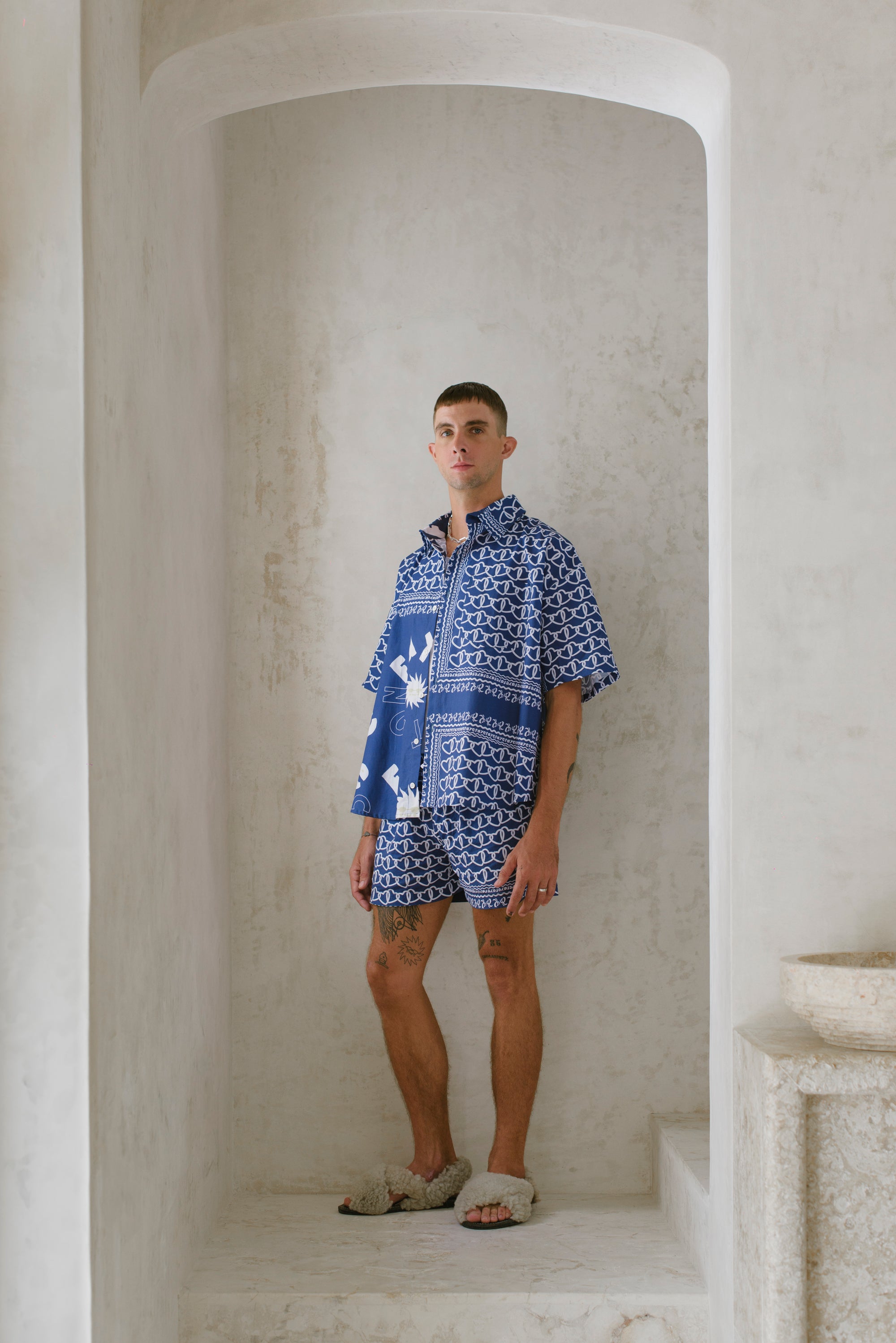 Man wearing a blue patterned shirt and shorts standing in a marble hallway.