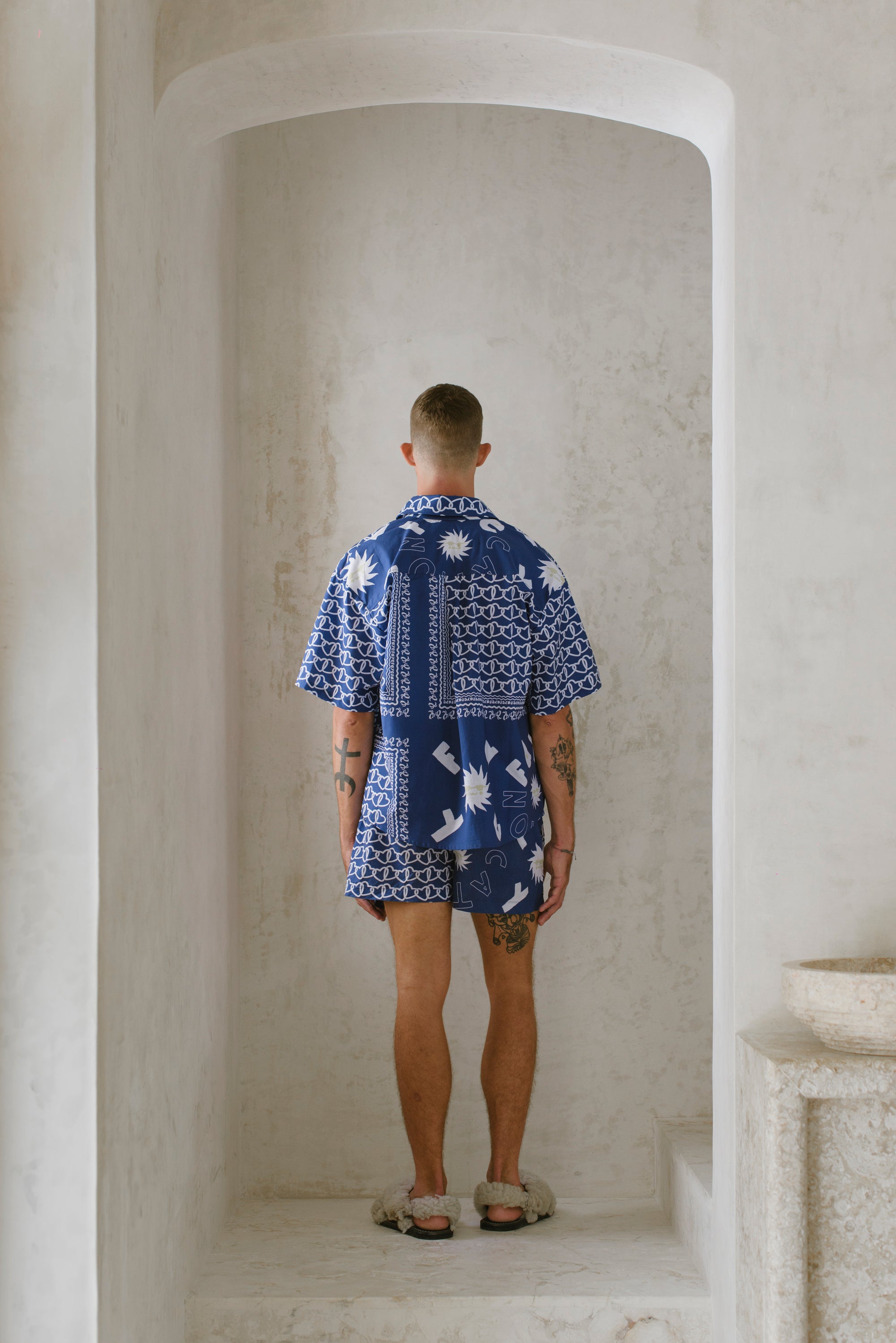 Man wearing a blue patterned shirt standing in a stone archway.