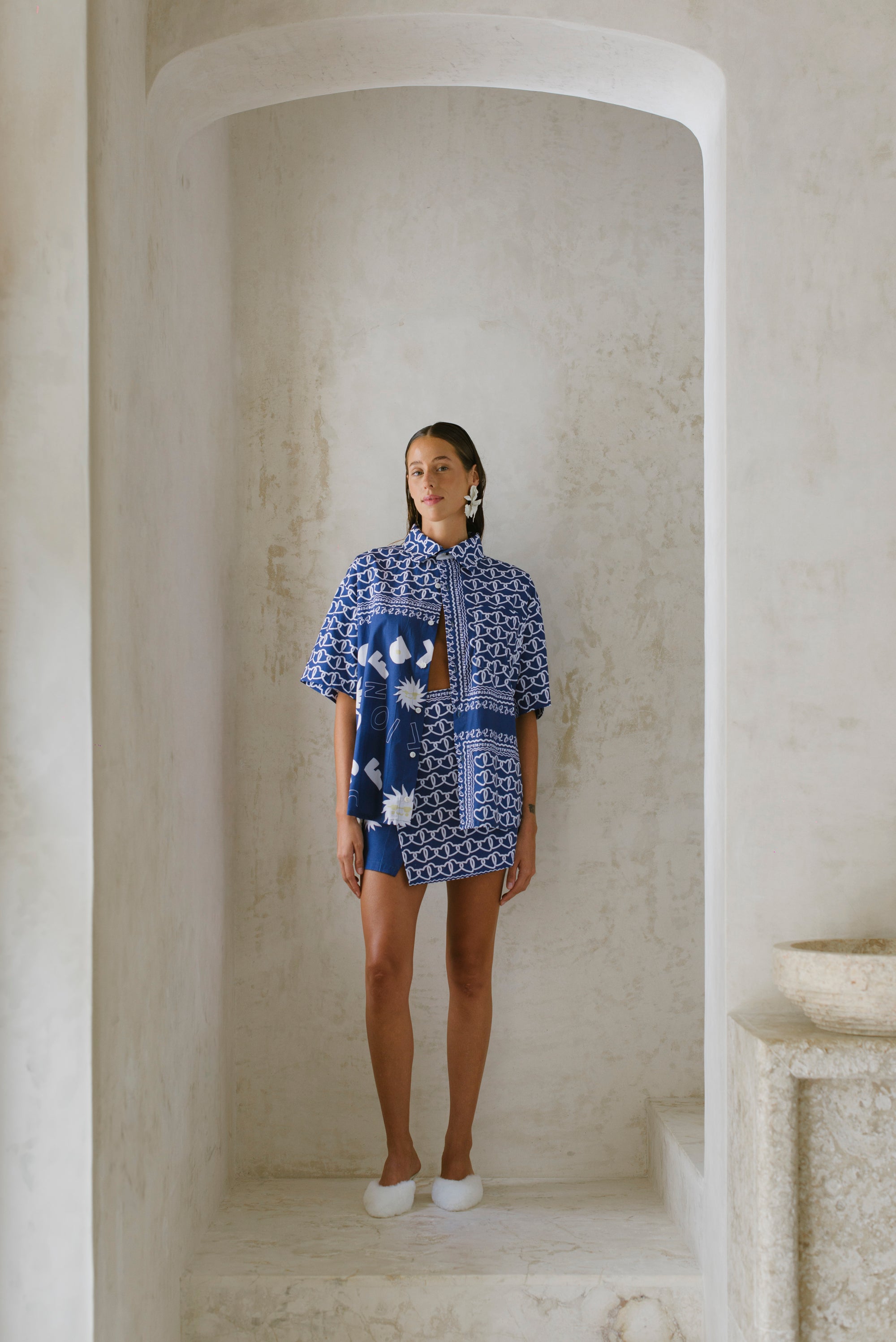 Woman wearing a blue patterned dress standing in a neutral-colored room.