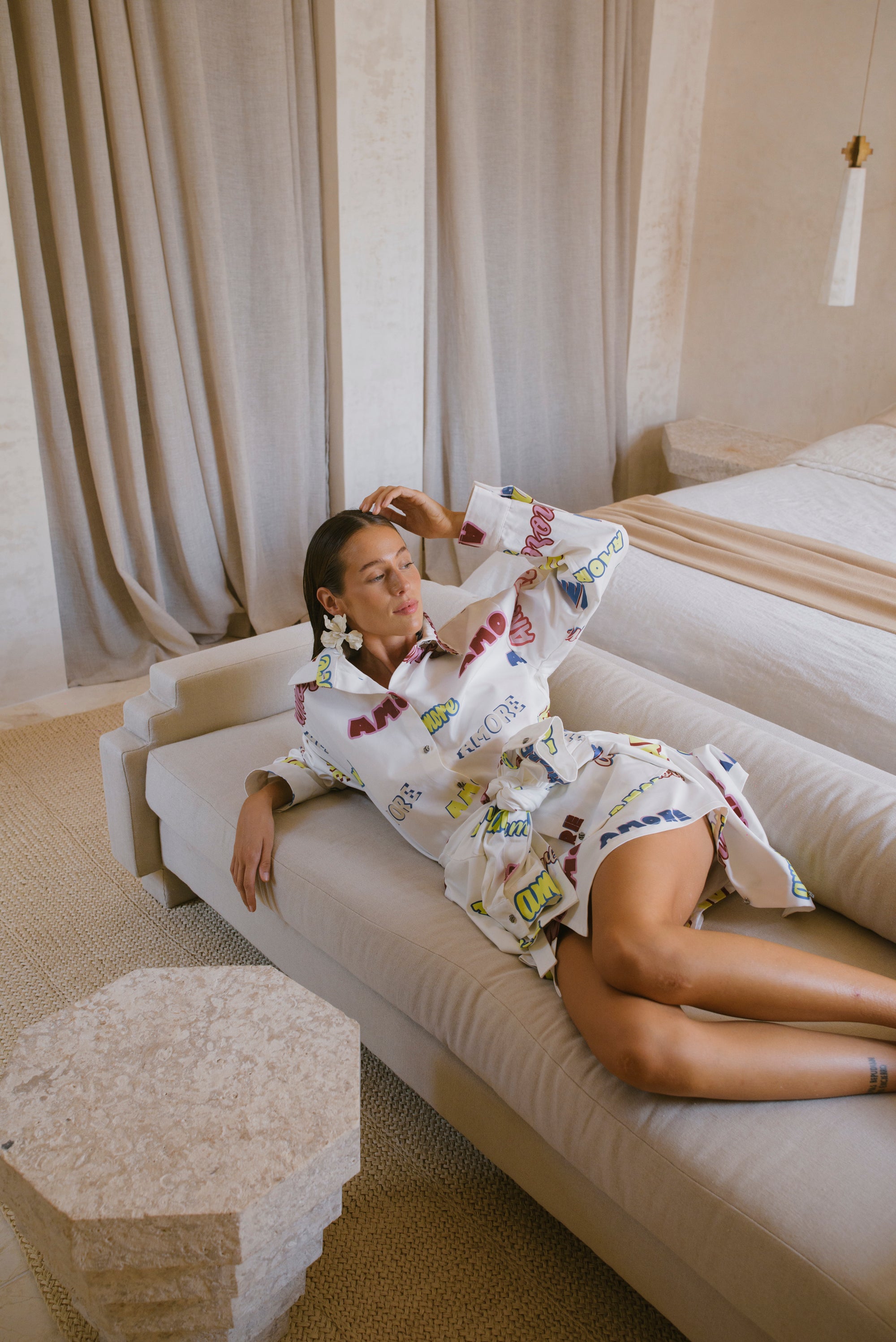 Woman in a patterned matching outfit lying on a white sofa in a stylish room.