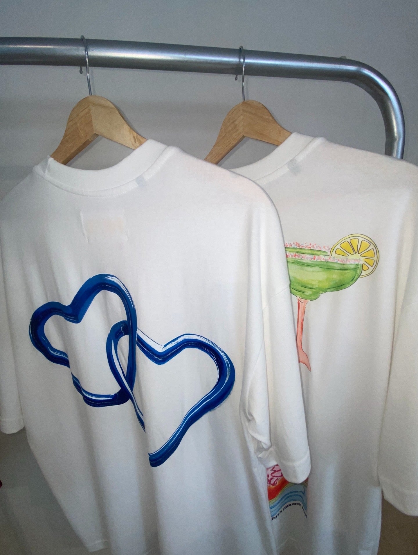 Two white sweatshirts on hangers with blue heart design and colorful graphic.