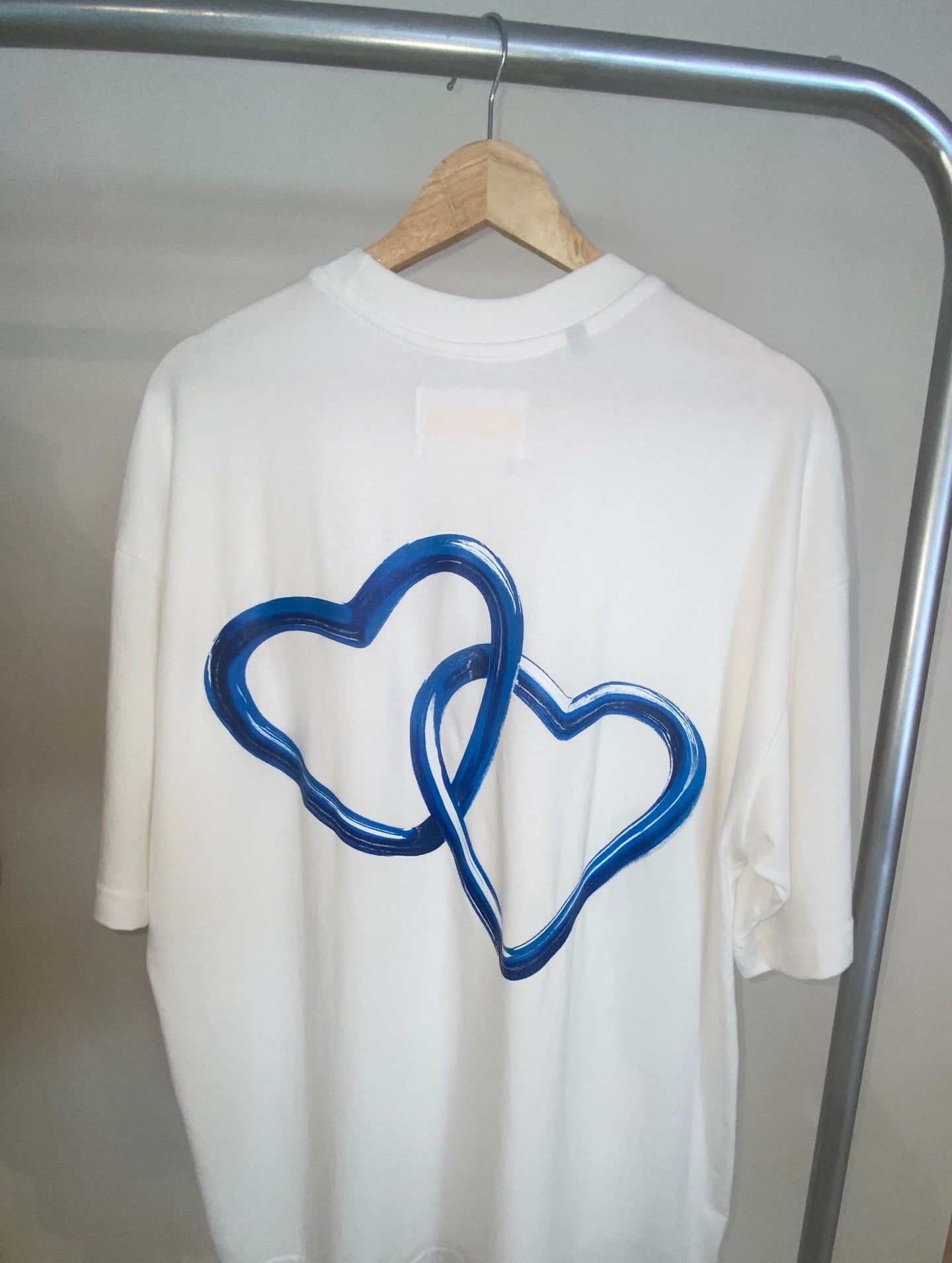 White shirt with blue heart design on a hanger against a neutral background