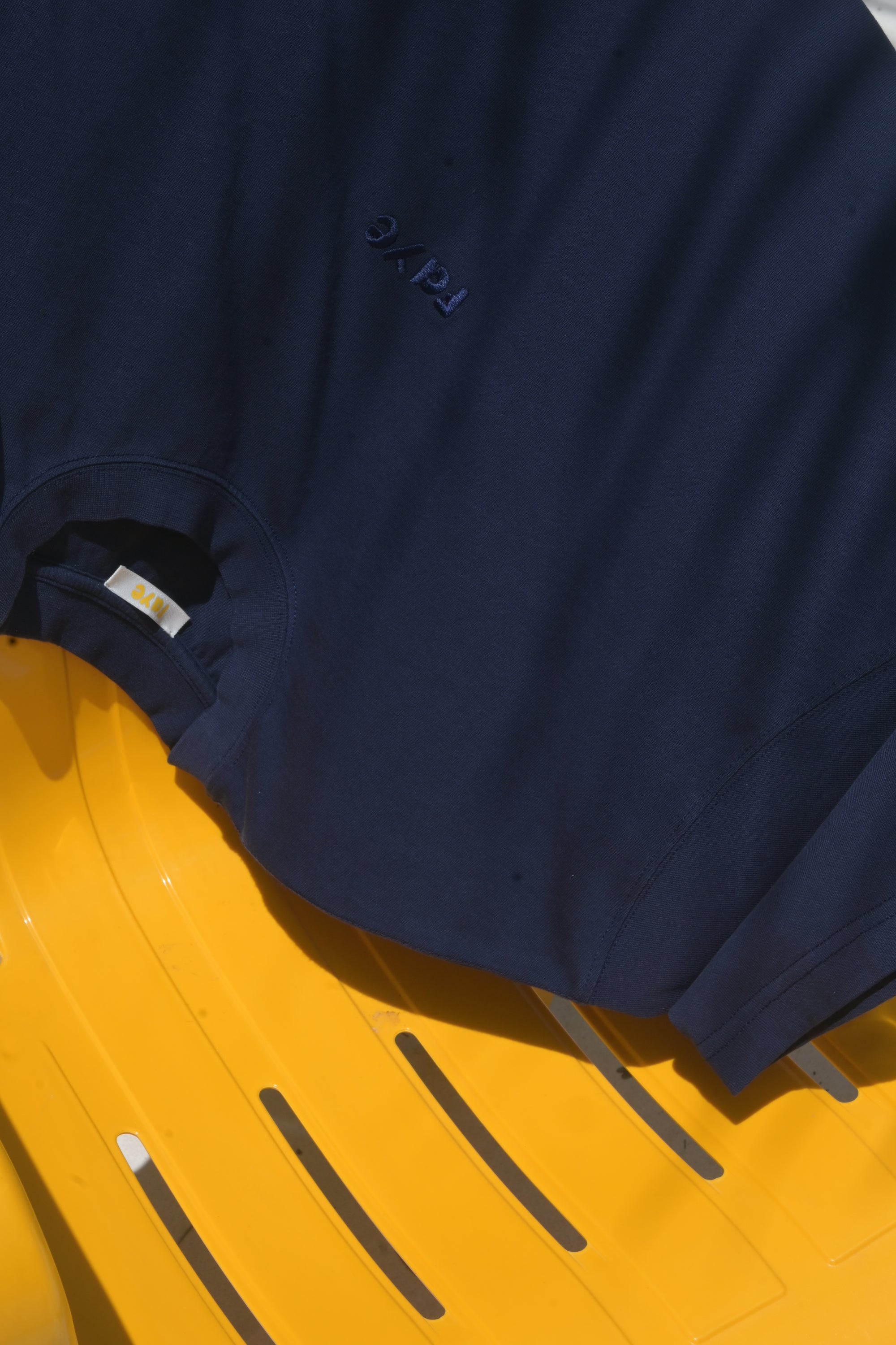 A close-up of a navy blue crewneck t-shirt laid flat on a bright yellow plastic surface.
