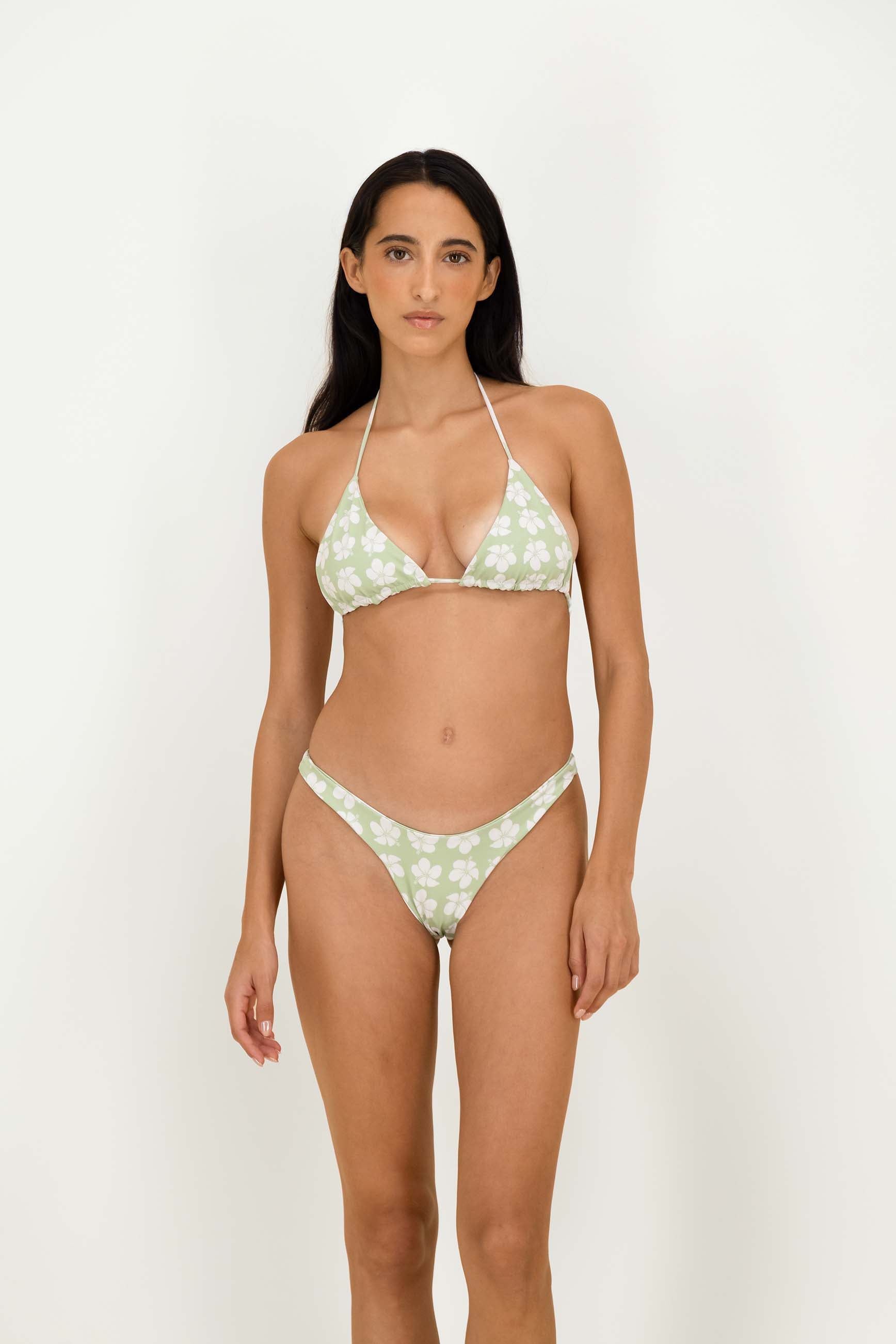 A woman modeling a two-piece bikini with a light sage green and white floral pattern against a plain white studio background.