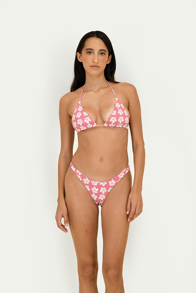 A woman modeling a two-piece bikini with a pink and white floral pattern against a plain light gray studio background.
