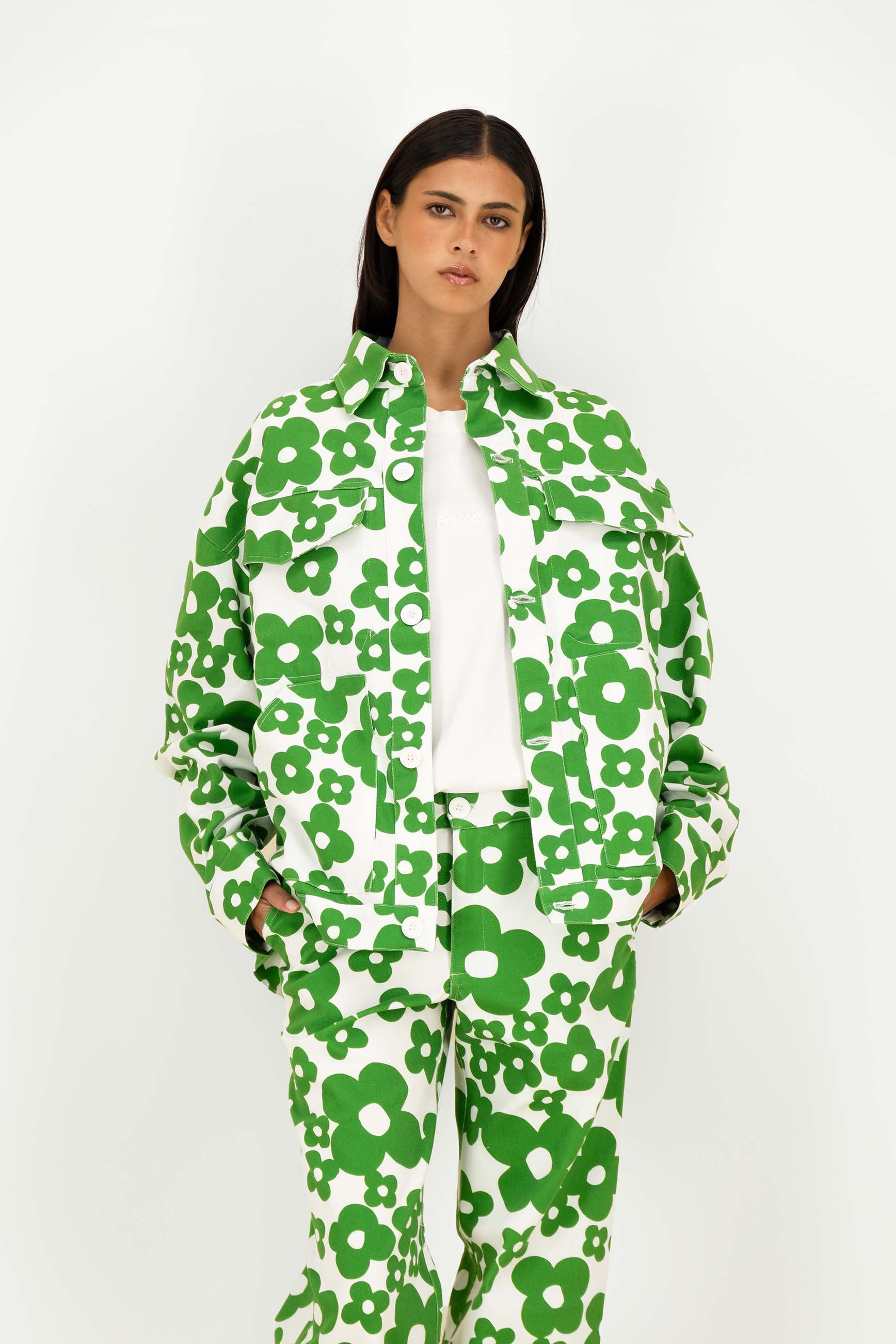 A model wearing a matching green and white floral print jacket and pants set over a white top, photographed against a plain light gray studio background.