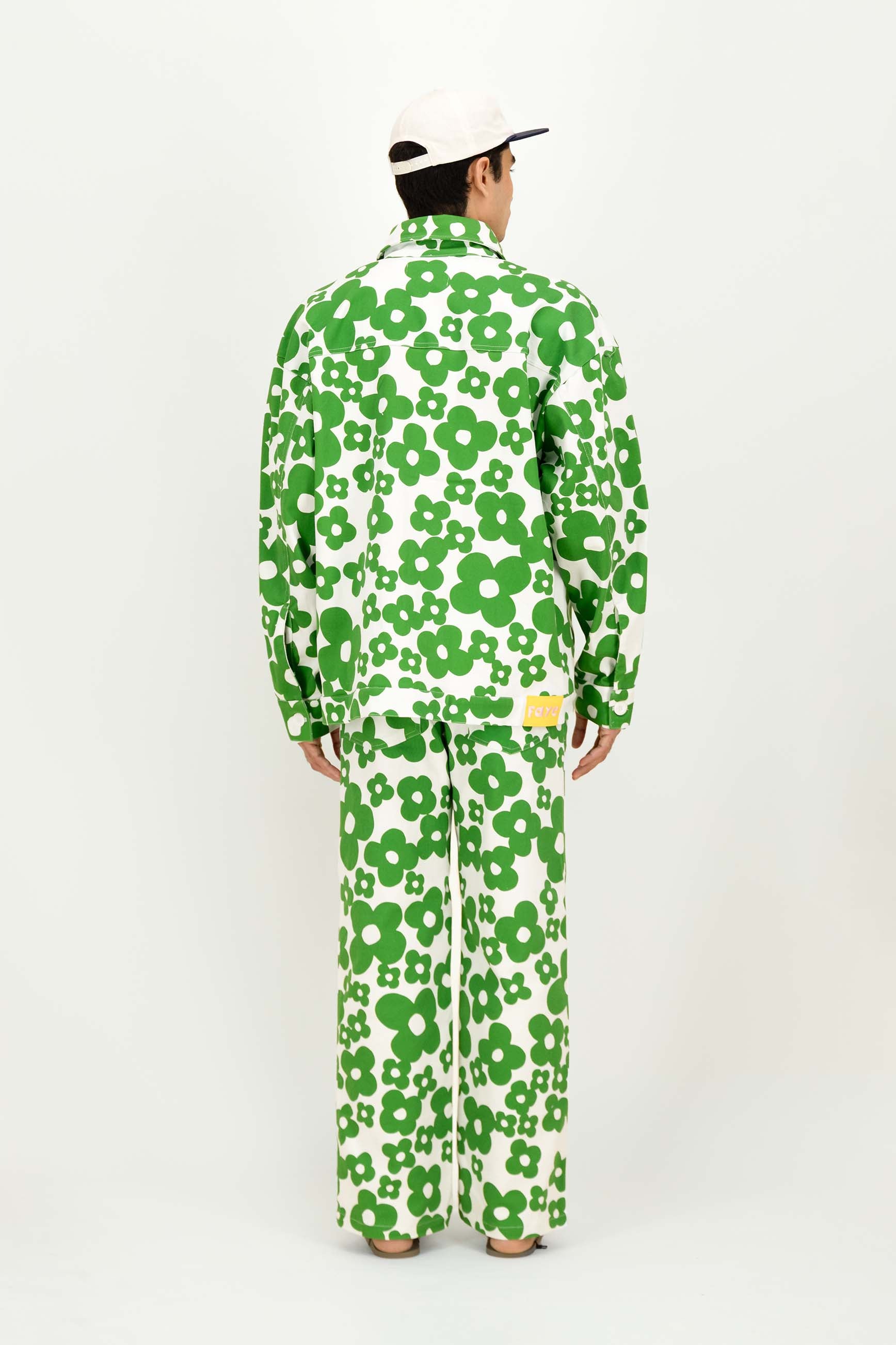 A man viewed from behind wearing a matching green and white floral print long-sleeve shirt and pants set, paired with a white cap, against a plain white studio background.