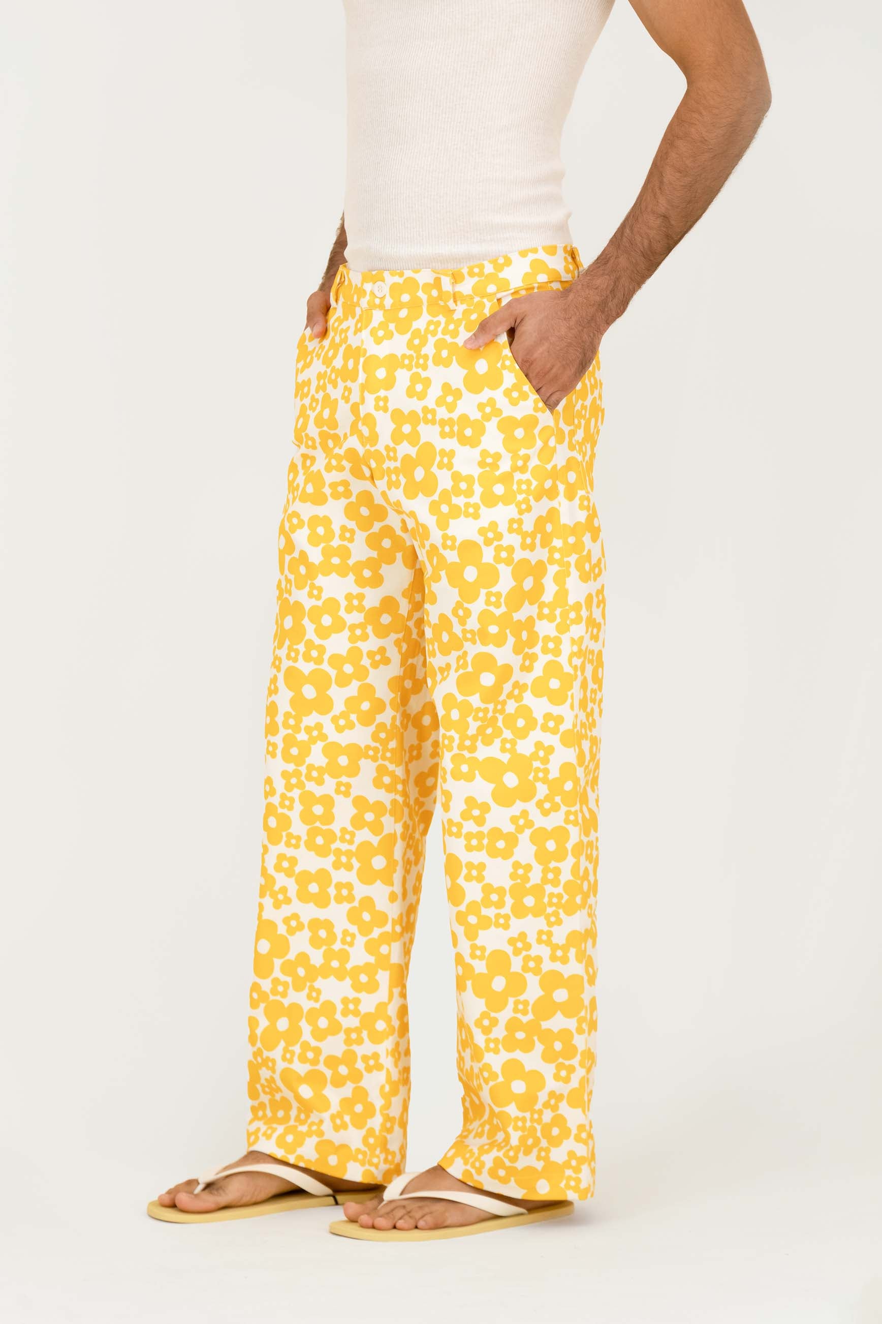 A person wearing yellow and white patterned wide-leg pants with a white tank top and tan sandals, shown from the waist down against a plain light background.