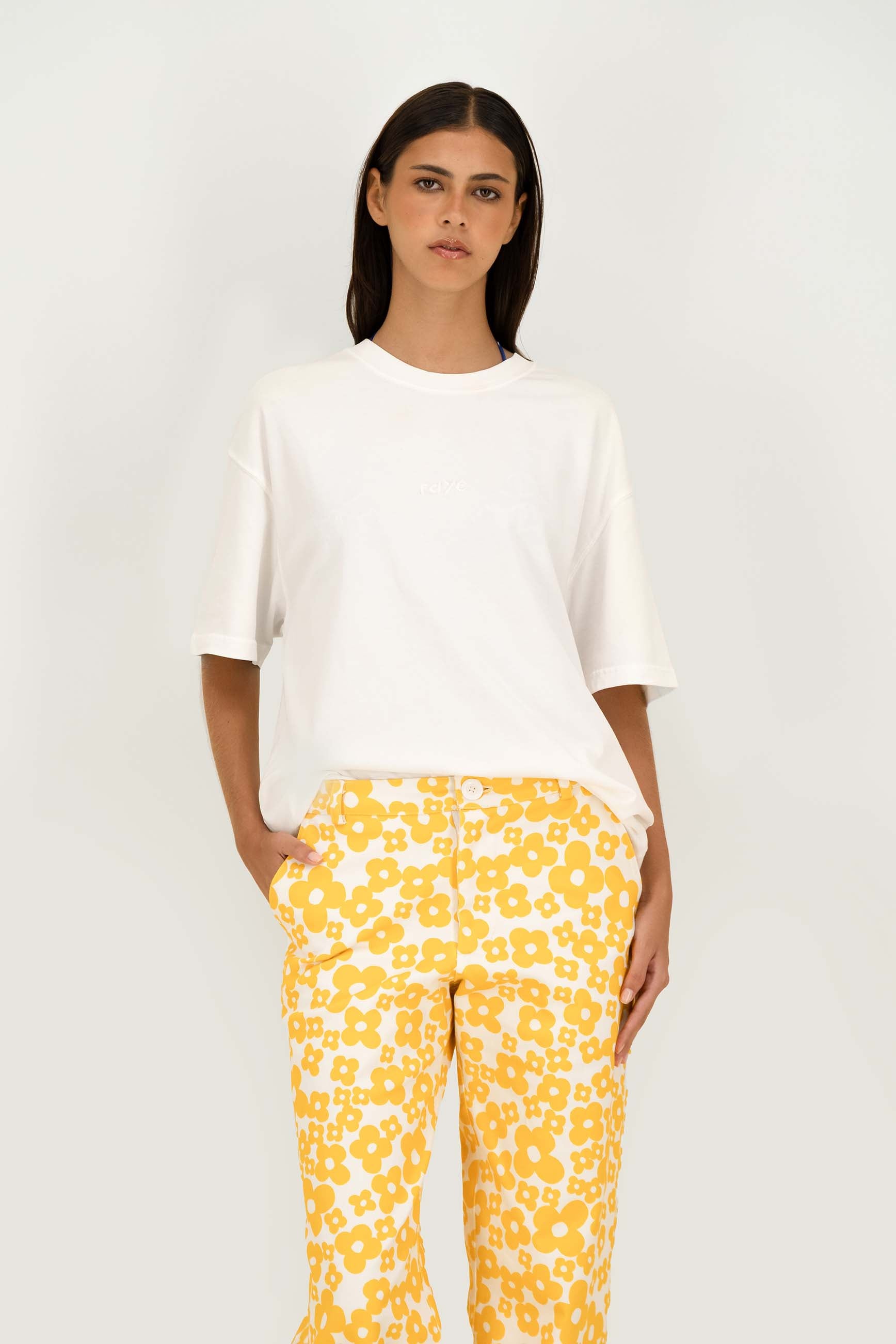A model wearing a white short-sleeve crewneck t-shirt and yellow-and-white floral print pants, standing against a plain white studio background.