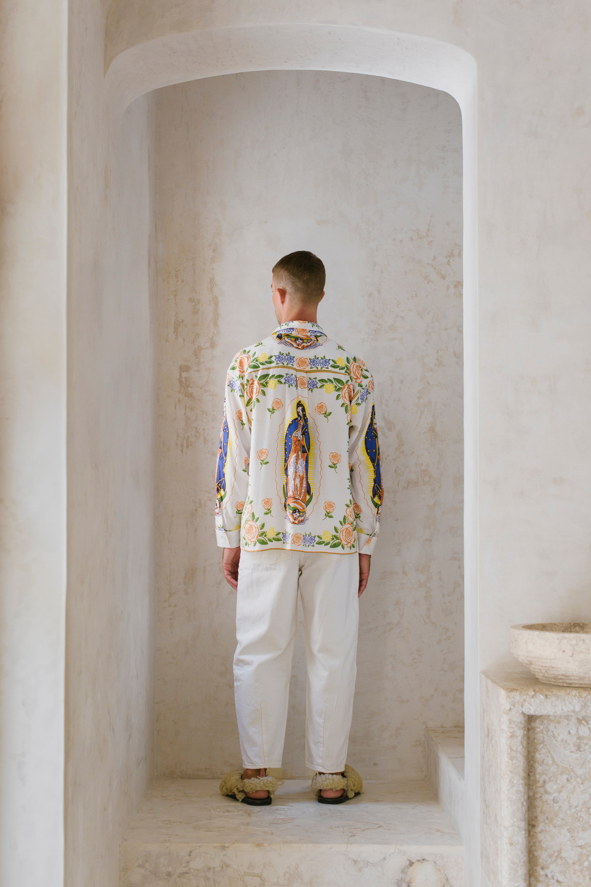 Person wearing a colorful printed shirt standing in a neutral-colored room.
