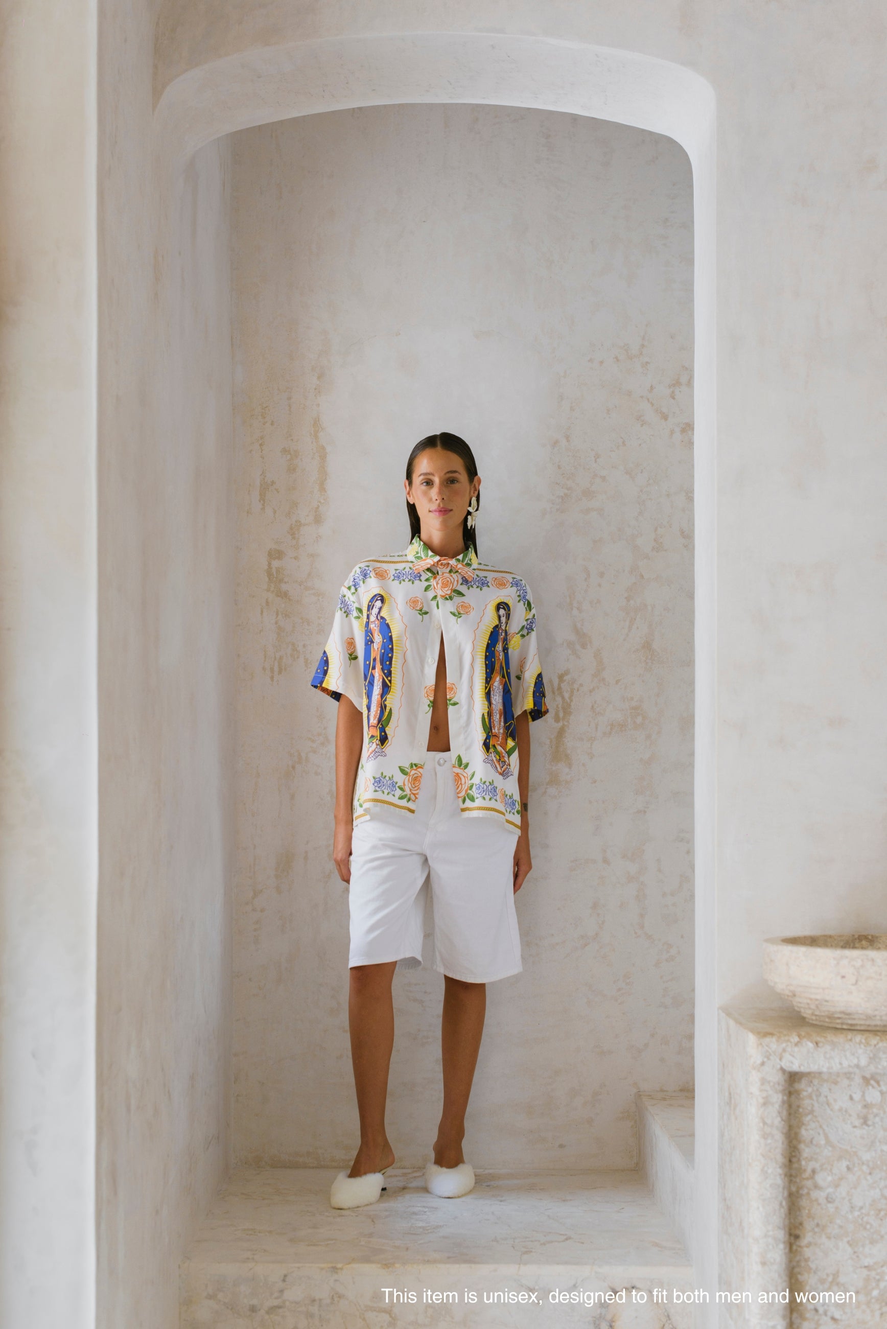 Person wearing a colorful printed shirt and white shorts standing in a stone archway.
